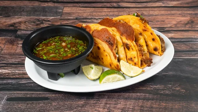 Quesabirria tacos with consomé and lime wedges at Tacos Nicole